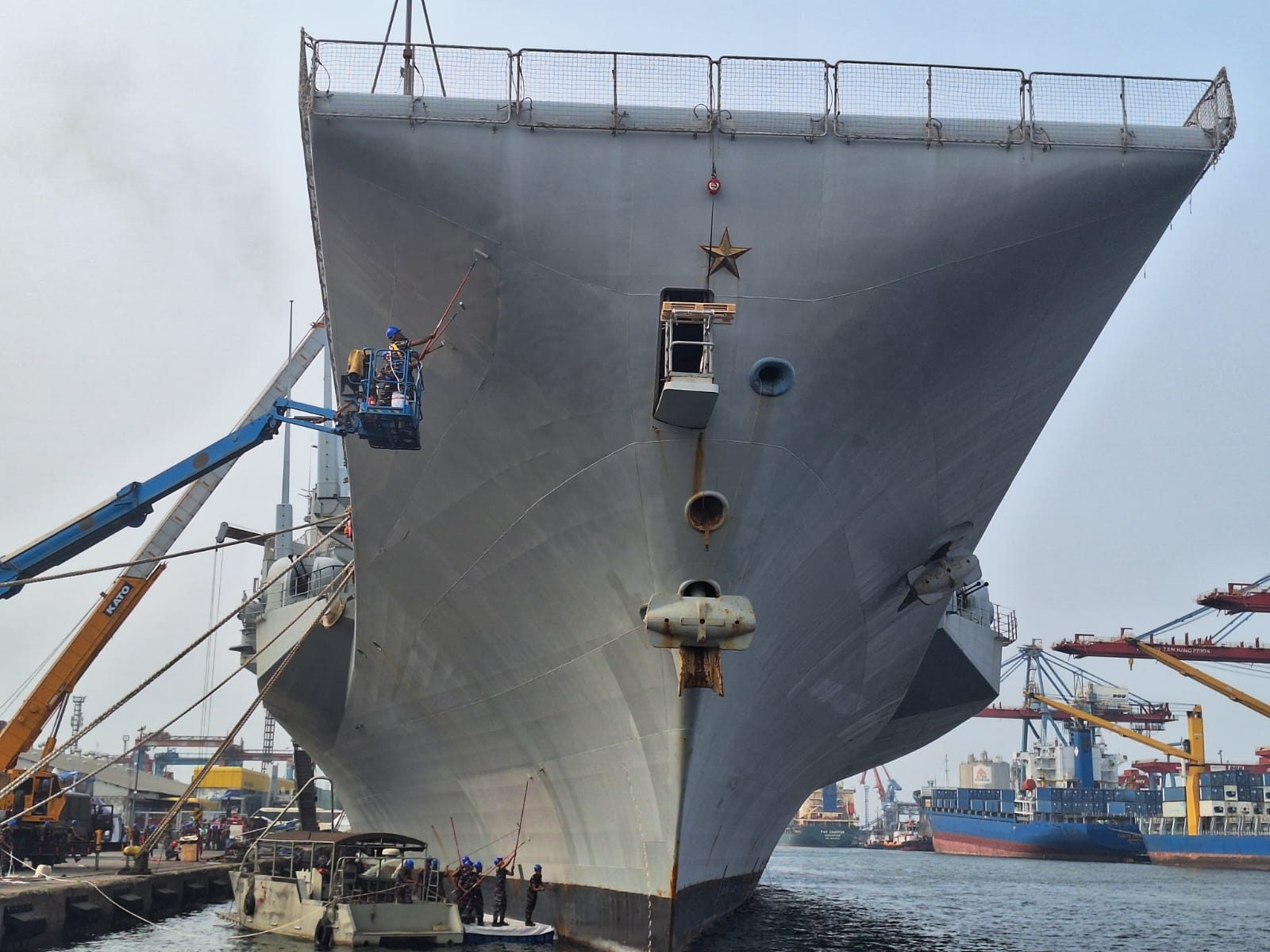 Naval vessel alongside, bow view with a painter on a boom lift